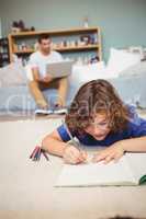 Boy writing in book while father working in background