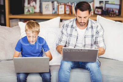 Father and son working on laptop at sofa