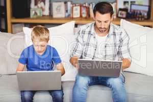 Father and son working on laptop at sofa