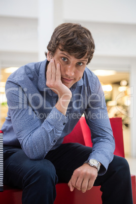 Man sitting in shopping mall with bored expression