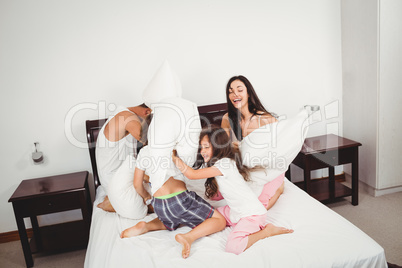 Family pillow fighting on bed against wall