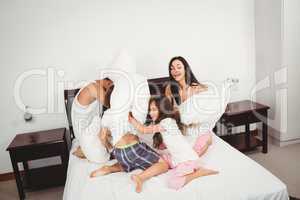 Family pillow fighting on bed against wall