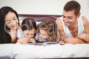 Happy children reading book with parents on bed