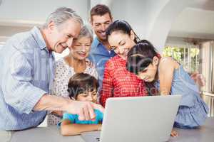 Senior man pointing on laptop while standing with family