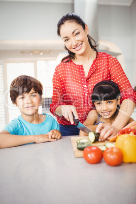 Woman standing with children by table while chopping vegetable