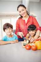 Woman standing with children by table while chopping vegetable