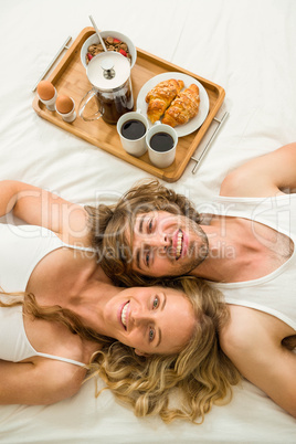 Cute couple lying in bed next to a breakfast tray