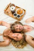 Cute couple lying in bed next to a breakfast tray