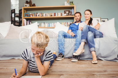 Boy drawing on paper while parents looking at him