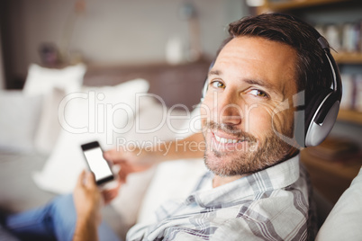 Smiling man wearing headphones while sitting on sofa