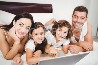 Portrait of happy children with parents using laptop on bed