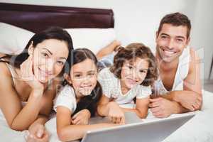 Portrait of happy children with parents using laptop on bed