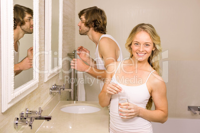 Blonde woman taking a pill with her boyfriend brushing his teeth