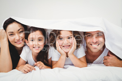 Cheerful family below blanket on bed