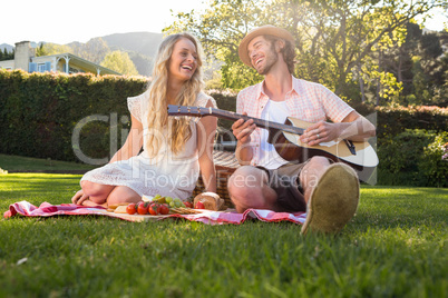 Happy couple having a picnic and playing guitar