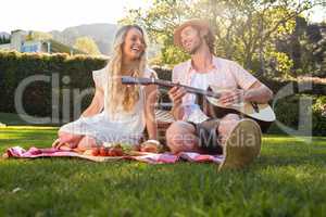 Happy couple having a picnic and playing guitar