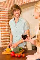 Cute couple enjoying a glass of wine and slicing vegetables
