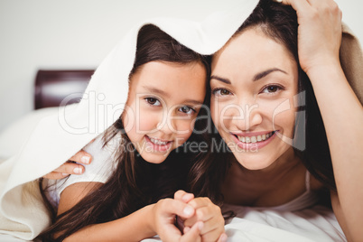 Portrait of mother and daughter below blanket on bed