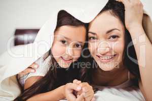 Portrait of mother and daughter below blanket on bed