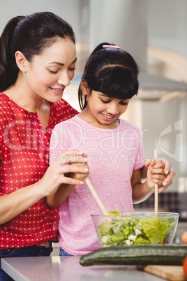 Smiling mother and daughter preparing salad