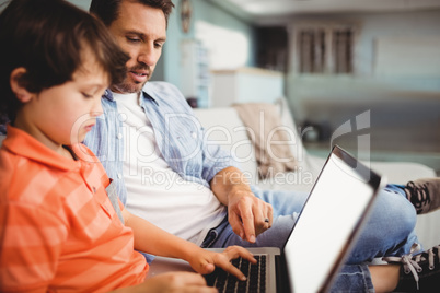 Father and son working on laptop while sitting on sofa