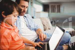 Father and son working on laptop while sitting on sofa