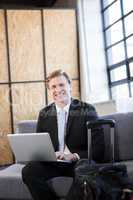 Happy businessman sitting on sofa and using laptop