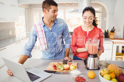 Couple standing with fruit juice while using laptop