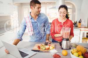 Couple standing with fruit juice while using laptop