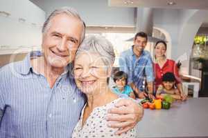 Portrait of senior couple with family preparing food in backgrou