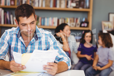 Man reading documents while family sitting in background