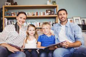 Portrait of cheerful family with book while sitting on sofa