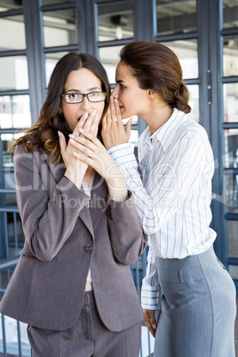 Businesswomen whispering in to her colleague ear