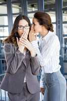 Businesswomen whispering in to her colleague ear