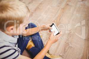 Boy using mobile phone while sitting on hardwood floor