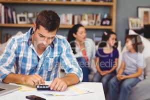 Serious man using calculator while family sitting in background