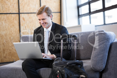 Happy businessman sitting on sofa and using laptop