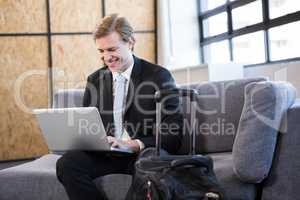 Happy businessman sitting on sofa and using laptop
