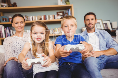 Smiling siblings playing video games with parents