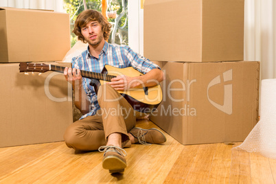 Handsome man playing guitar with moving boxes
