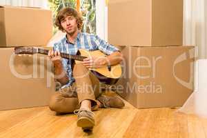 Handsome man playing guitar with moving boxes