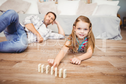 Happy girl arranging domino by father on hardwood floor