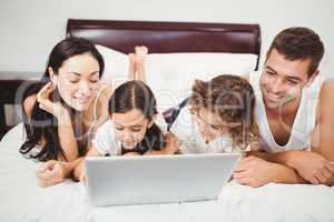 Happy children with parents using laptop on bed
