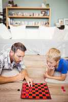 Father and son playing checker game at home