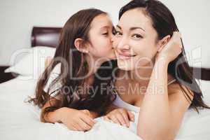 Cute daughter kissing mother on bed at home