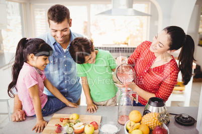 Happy family with mother pouring fruit juice in jug