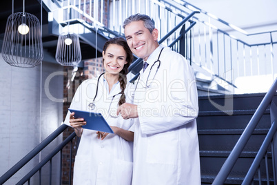 Portrait of happy doctors holding digital tablet on staircase
