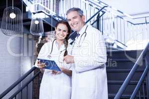 Portrait of happy doctors holding digital tablet on staircase