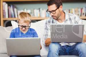 Father and son with eyeglasses while working on laptop