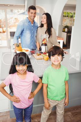 Siblings standing at table with parents preparing fruit juice